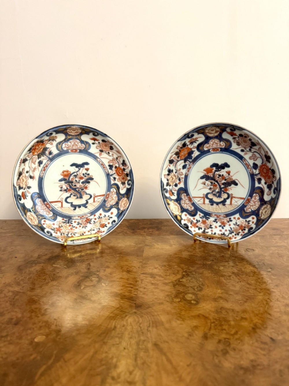 A pair of circular 19th-century Japanese Imari porcelain plates decorated with floral motifs in underglaze cobalt blue, iron-red enamel, and gilded highlights.
