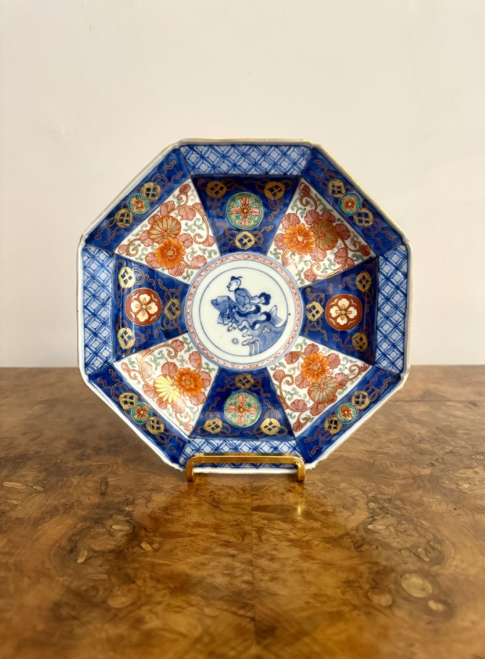 An antique Japanese hexagonal porcelain plate decorated with cobalt blue diaper patterns, iron-red floral motifs, and a central roundel featuring a human figure.