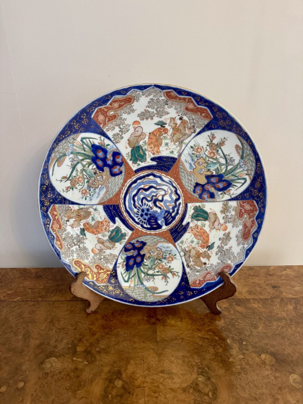 A large circular Japanese Imari porcelain charger featuring segmented panels decorated with floral patterns, human figures, and a central medallion motif in cobalt blue, iron red, and gilt details.
