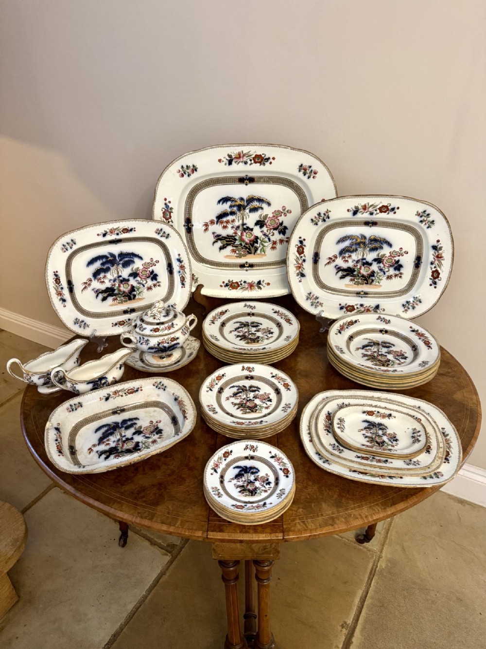 An antique Victorian Wedgwood earthenware part dinner service featuring graduated serving platters, dinner plates, a sauce tureen, and gravy boats with polychrome botanical and tree motifs.