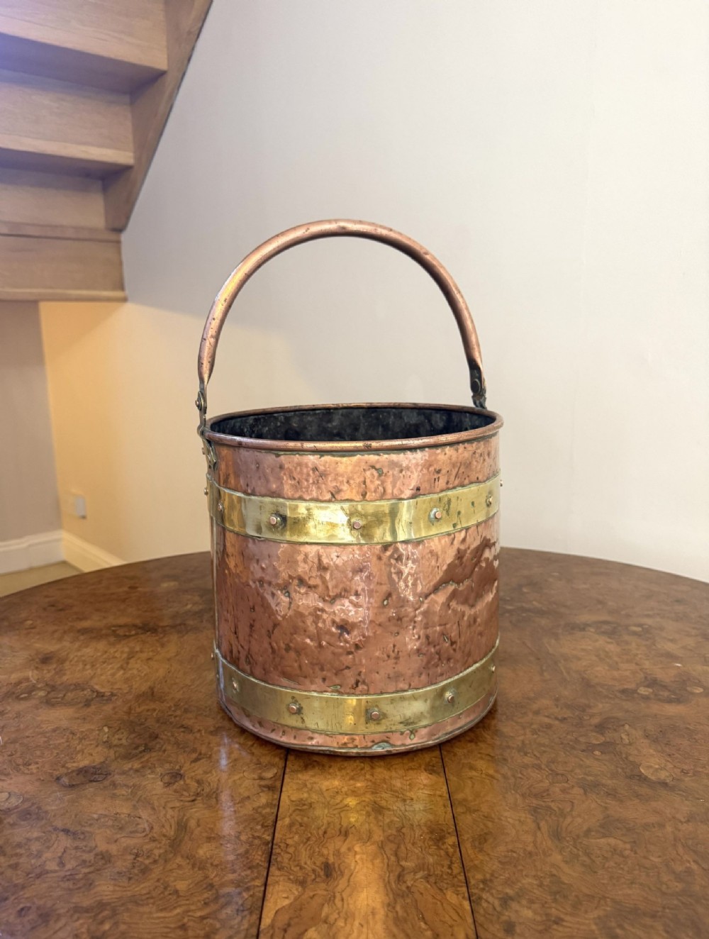 A Victorian hammered copper coal bucket featuring decorative brass banding, metal rivets, and an overhead swing handle.