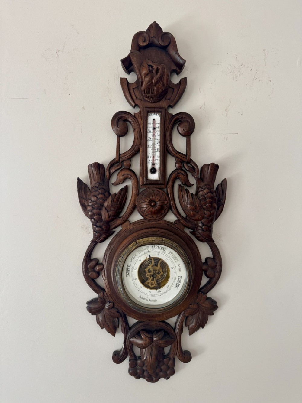 A deeply carved dark wood Victorian Black Forest aneroid barometer featuring game bird and foliage motifs with an integrated thermometer.