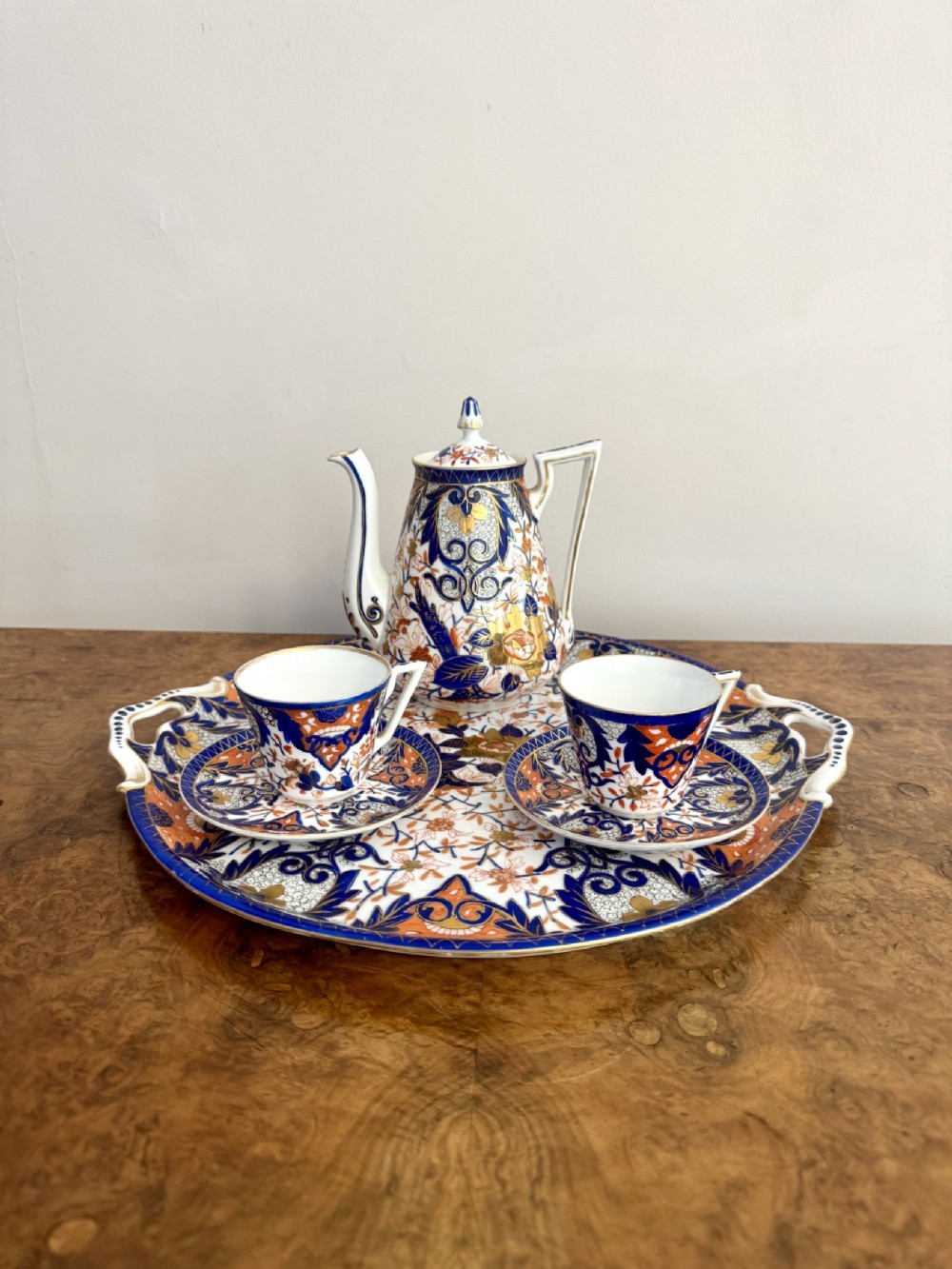 A nineteenth-century porcelain coffee set decorated in an Imari pattern of cobalt blue, orange, and gilt, arranged on a matching twin-handled oval porcelain tray.