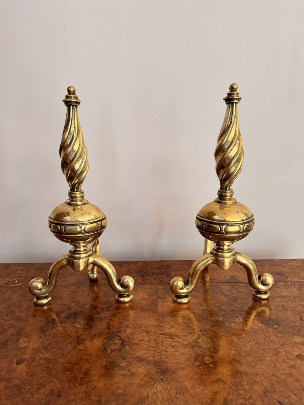 A pair of Victorian solid brass fire dogs featuring spiral turned finials, central knops, and scrolled tripod feet.
