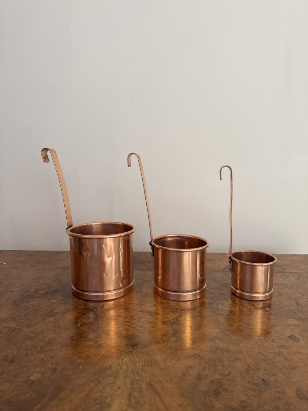 A set of three graduated Victorian copper liquid measures featuring cylindrical bodies and long vertical handles with curved hooks.