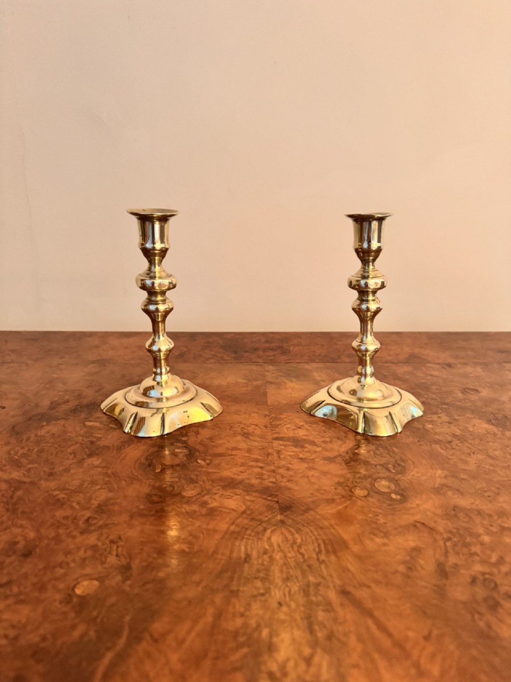 A pair of gold brass Queen Anne candlesticks featuring turned baluster stems and shaped scalloped bases.