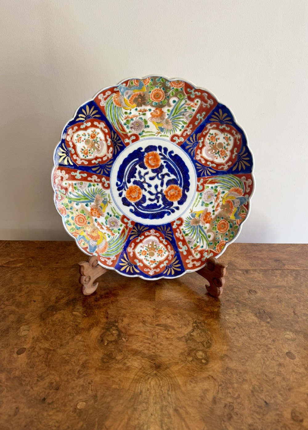 A large circular antique Japanese Imari porcelain charger featuring a scalloped rim, cobalt blue centre medallion, and segmented panels painted with phoenix birds and floral motifs in red, blue, and gold.