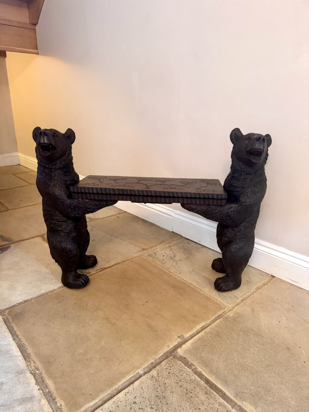A dark brown carved wooden bench supported by two standing sculpted bears holding a central rectangular seat with carved leaf patterns.