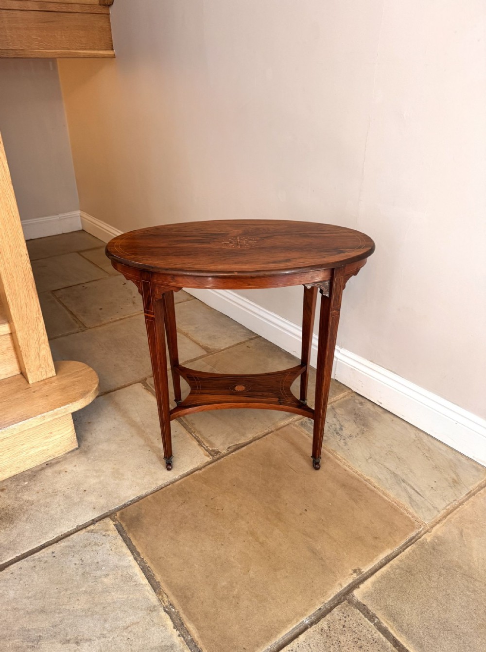An Edwardian oval mahogany occasional table featuring central marquetry inlays, satinwood line stringing, four square tapered legs, and an arched lower undertier.