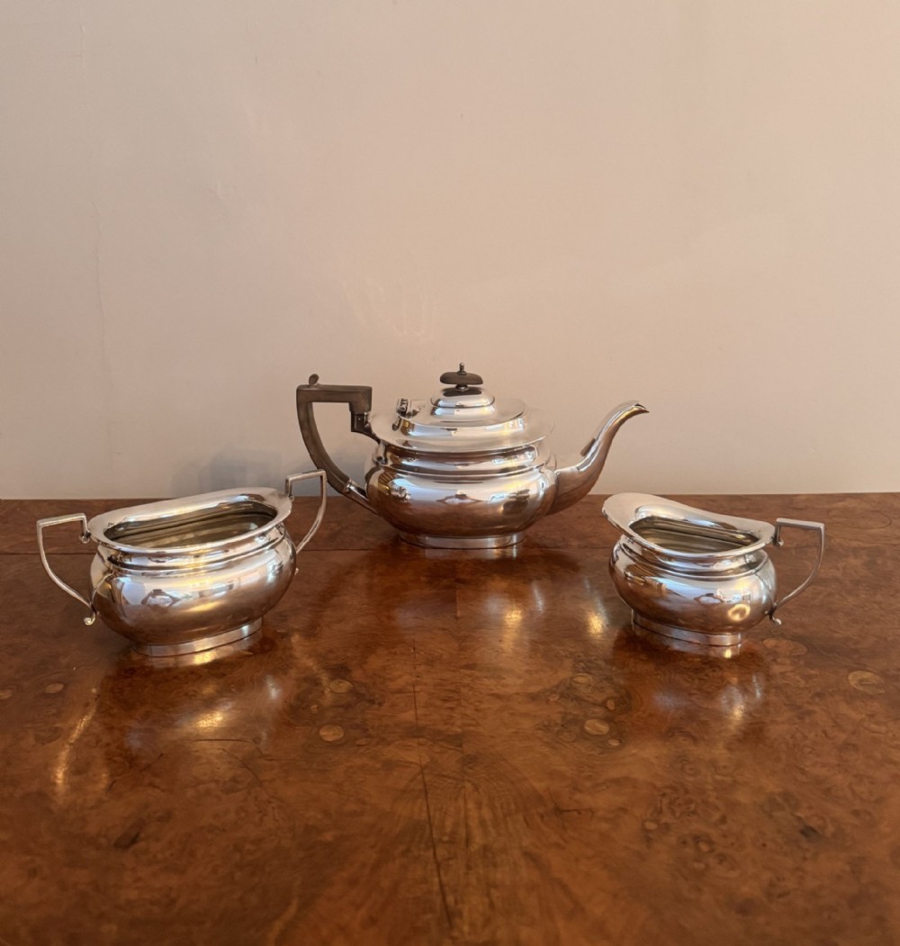 A three-piece Edwardian silver-plated tea set comprising a teapot with an ebonised wooden handle, a sugar bowl, and a milk jug.