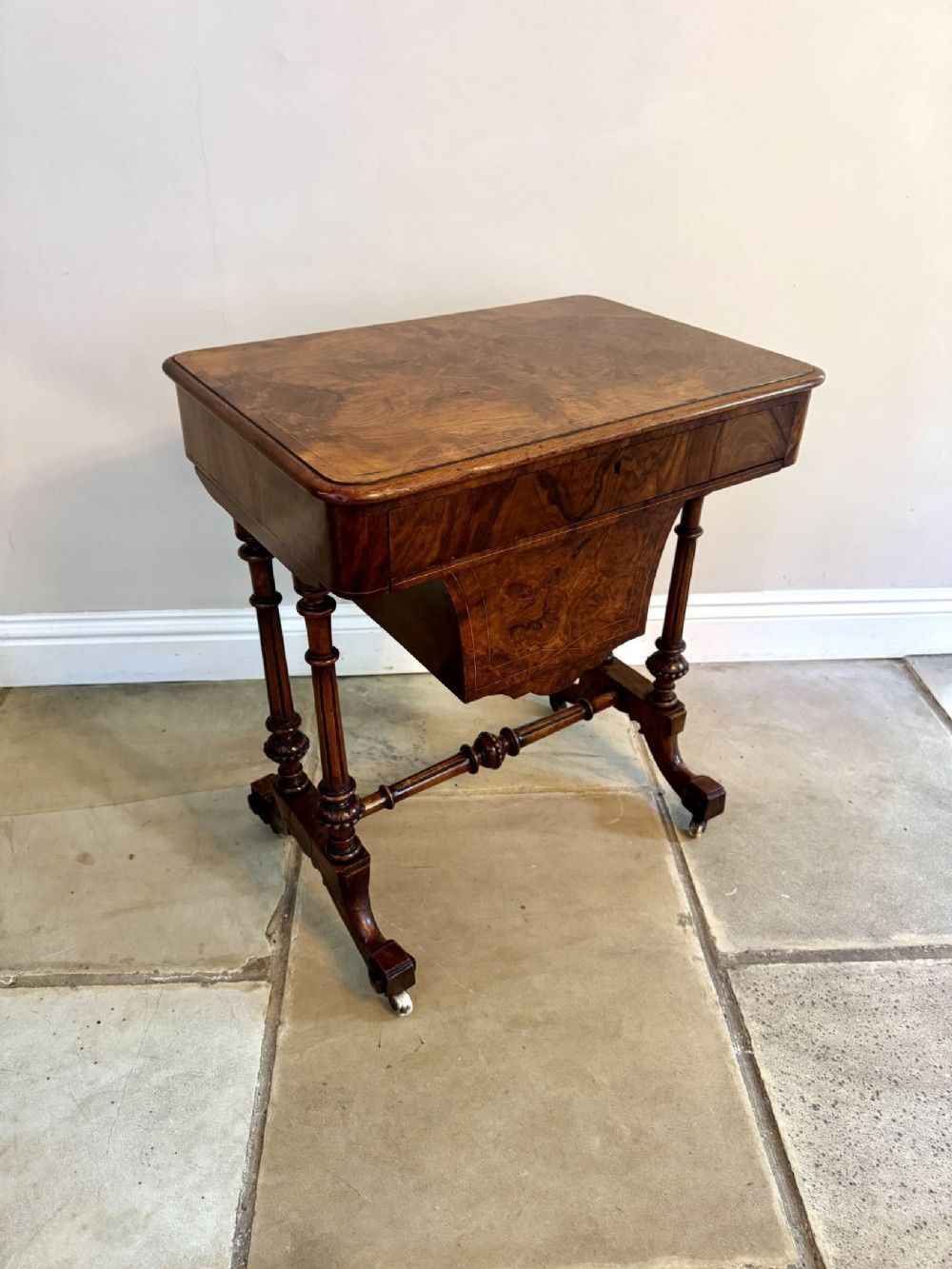 A Victorian burr walnut work table featuring a rectangular top, lowered storage well, turned twin supports, stretcher base, and ceramic castors.