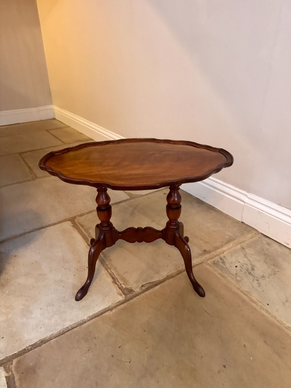 A Victorian mahogany occasional table featuring a scalloped oval top supported by twin turned pedestals and splayed legs with a shaped cross-stretcher.