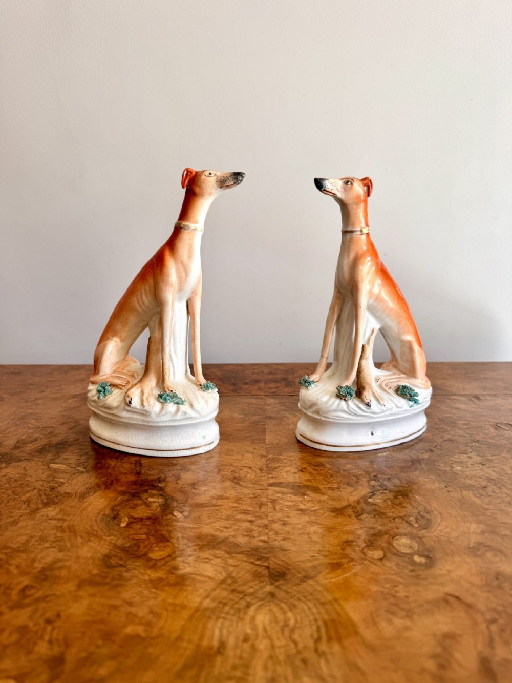A pair of Victorian Staffordshire earthenware greyhound figures painted in orange and white seated on oval decorative bases.