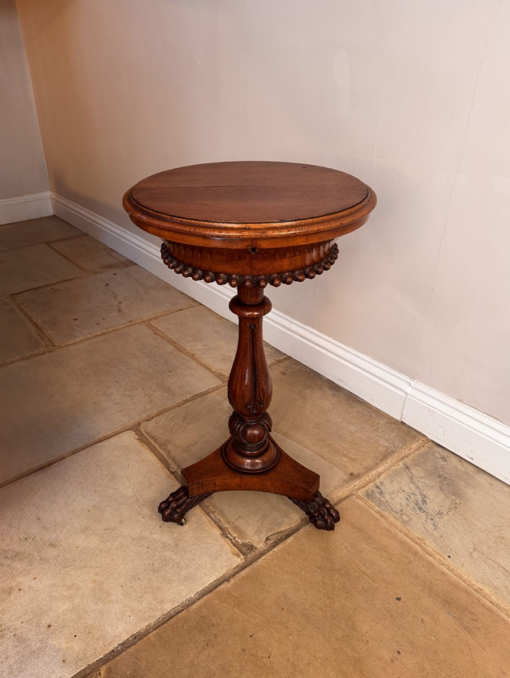 A circular Victorian oak work table featuring a carved turned stem and a tripod base with carved feet on castors.