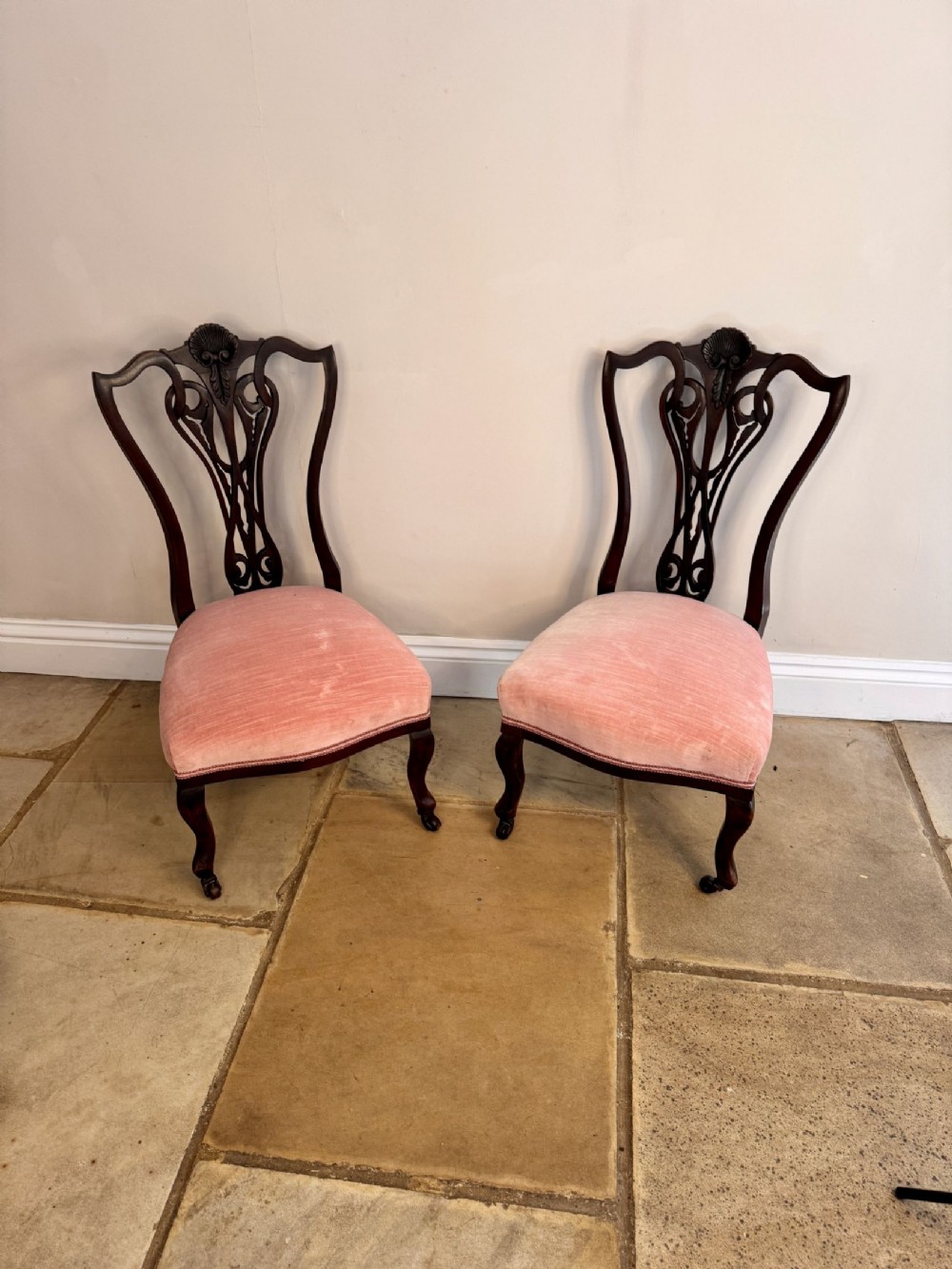 A pair of Victorian mahogany side chairs featuring carved openwork back splats, cabriole front legs, and pink velvet upholstered seats.