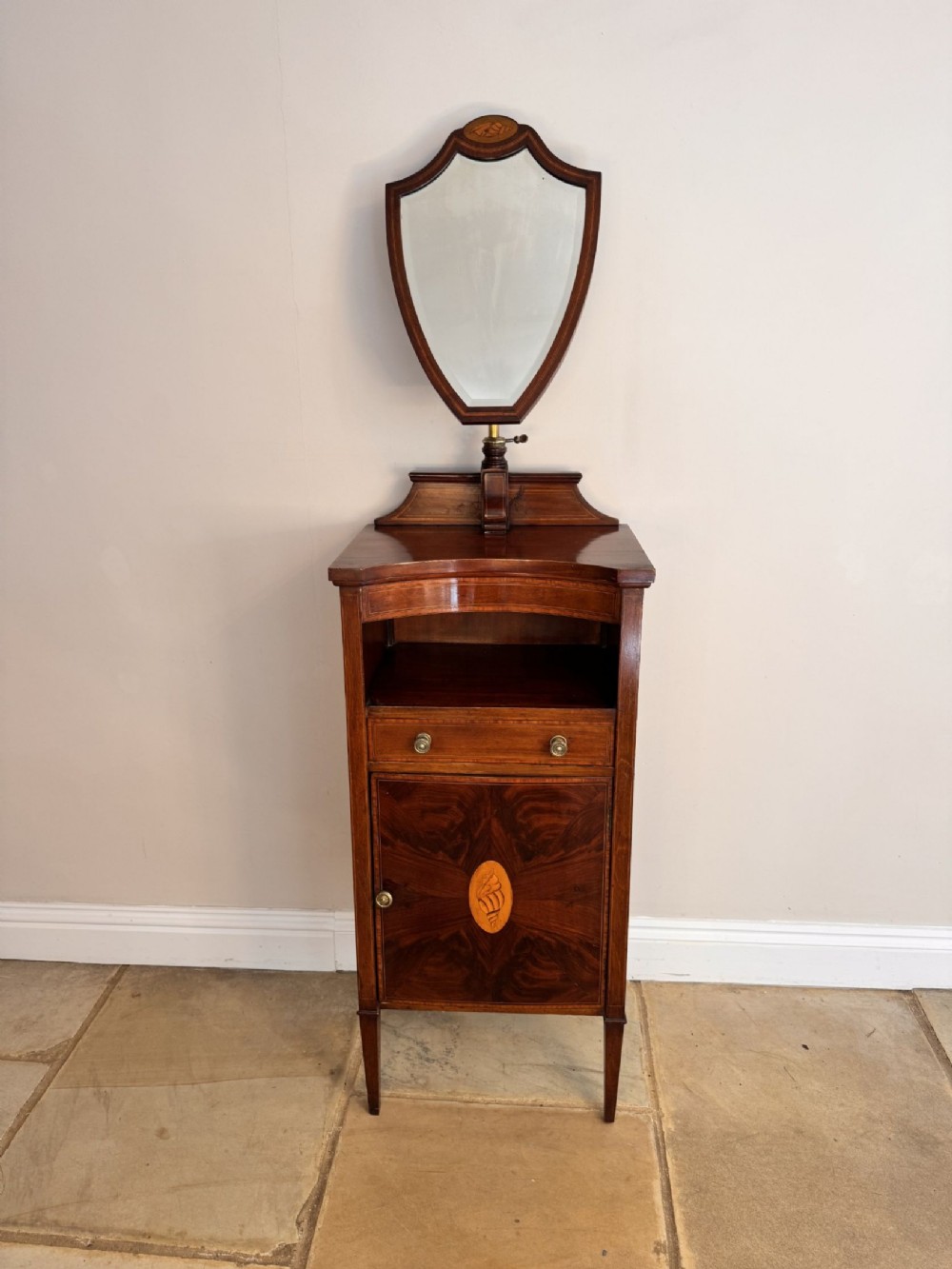 An Edwardian mahogany dressing stand featuring a shield-shaped adjustable mirror above an open shelf, drawer, and single cupboard with satinwood marquetry.