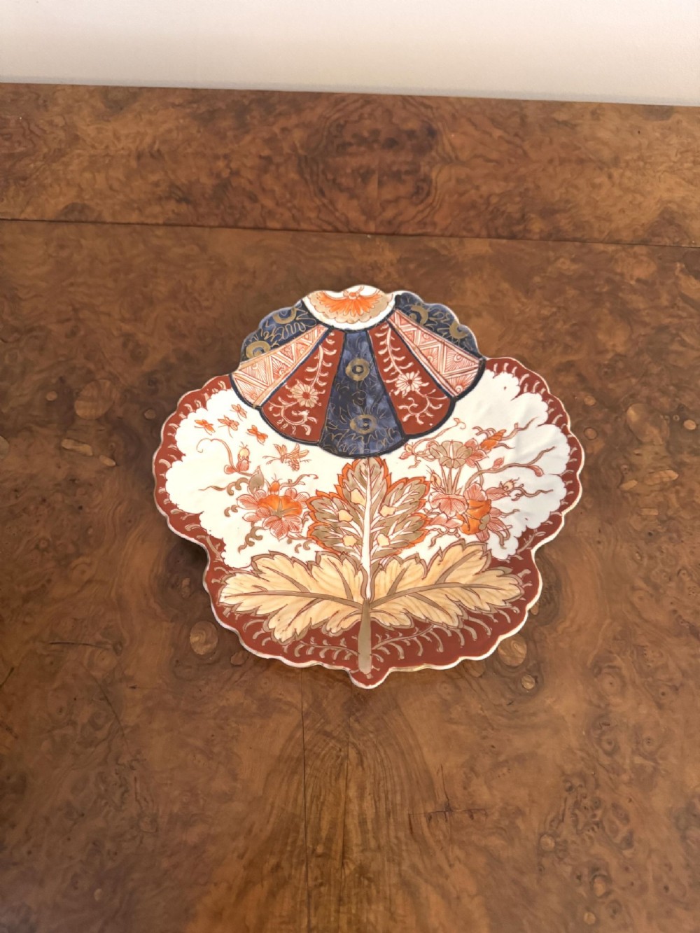 A Japanese Imari porcelain leaf-shaped dish decorated with iron-red, cobalt blue, and gilded floral motifs against a white background.