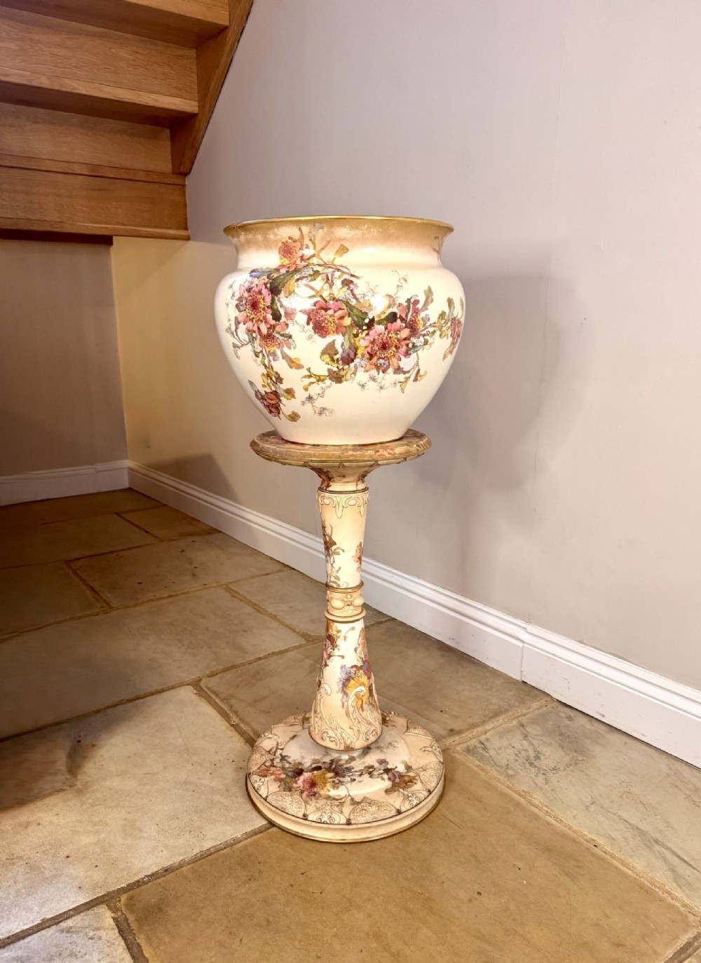 A late Victorian Royal Doulton ceramic jardiniere and matching tall pedestal decorated with hand-painted pink floral motifs, scrollwork, and gold leaf rim detailing.