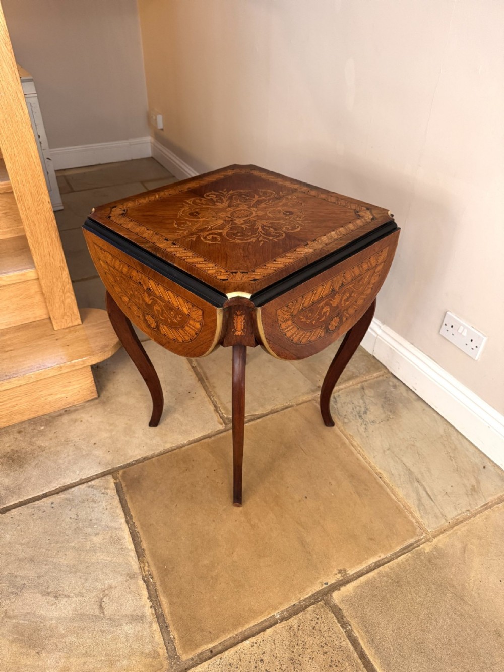 A 19th-century square wooden occasional table featuring floral marquetry inlay on the tabletop and drop flaps, supported by four slender cabriole legs with brass mounts.
