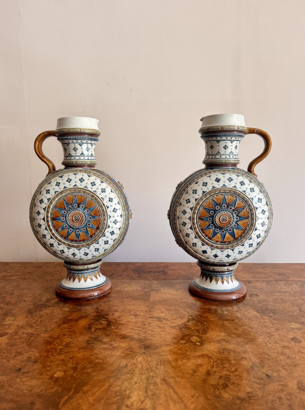A pair of 19th-century Villeroy and Boch stoneware ewers featuring circular disc-shaped bodies decorated with blue and ochre starburst medallions on elevated pedestal bases.