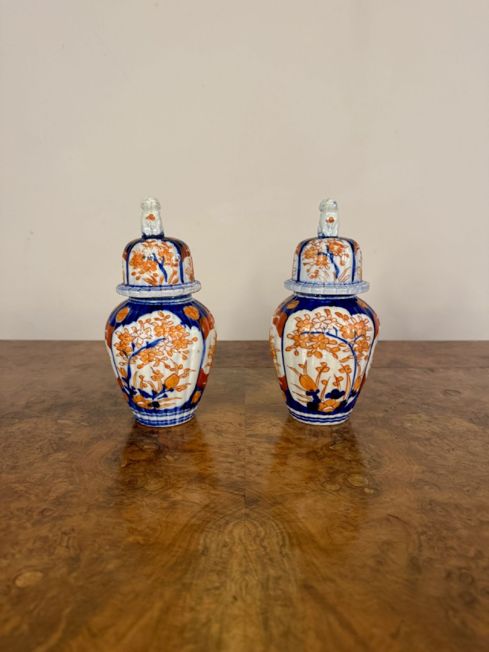 A pair of small antique Japanese Imari porcelain lidded vases decorated with orange and blue floral patterns and topped with sculpted shishi finials.
