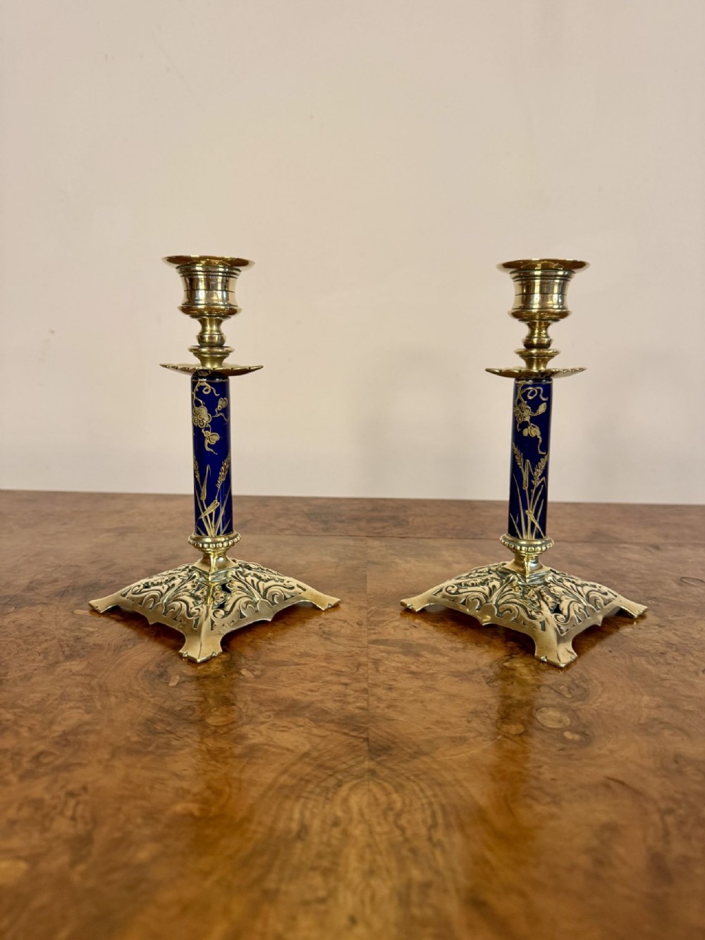 A pair of antique Victorian brass candlesticks featuring cobalt blue porcelain stems with gilt floral motifs and ornate scroll-cast square bases.