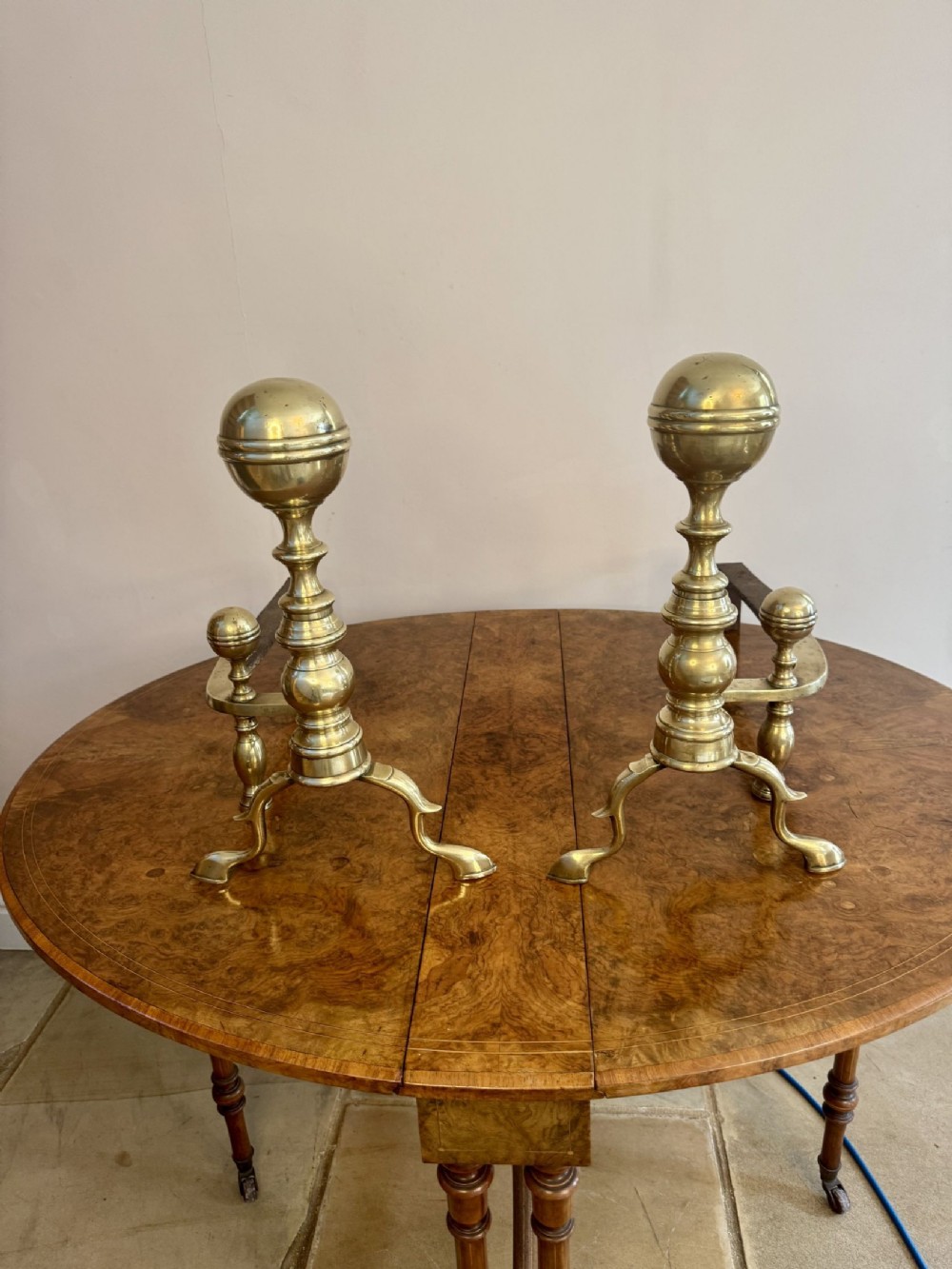 A pair of nineteenth-century brass fire dogs featuring spherical finials, turned baluster columns, and splayed legs resting on iron billets.