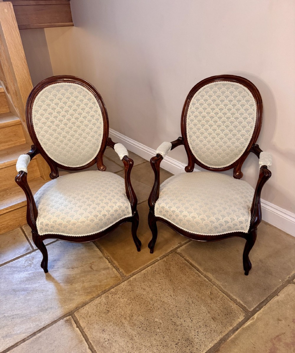 A pair of Victorian dark walnut armchairs featuring oval medallion backs, padded armrests, and carved cabriole legs upholstered in a light-coloured patterned textile.