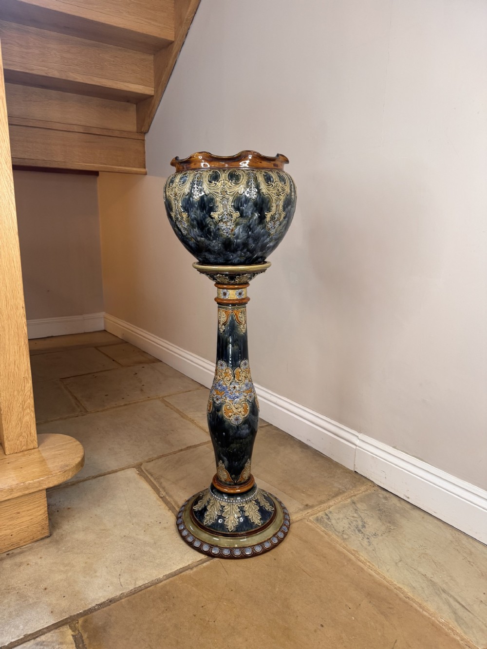 An Art Nouveau glazed stoneware jardiniere with foliate motifs positioned on a matching tall ceramic pedestal in shades of navy blue and ochre.