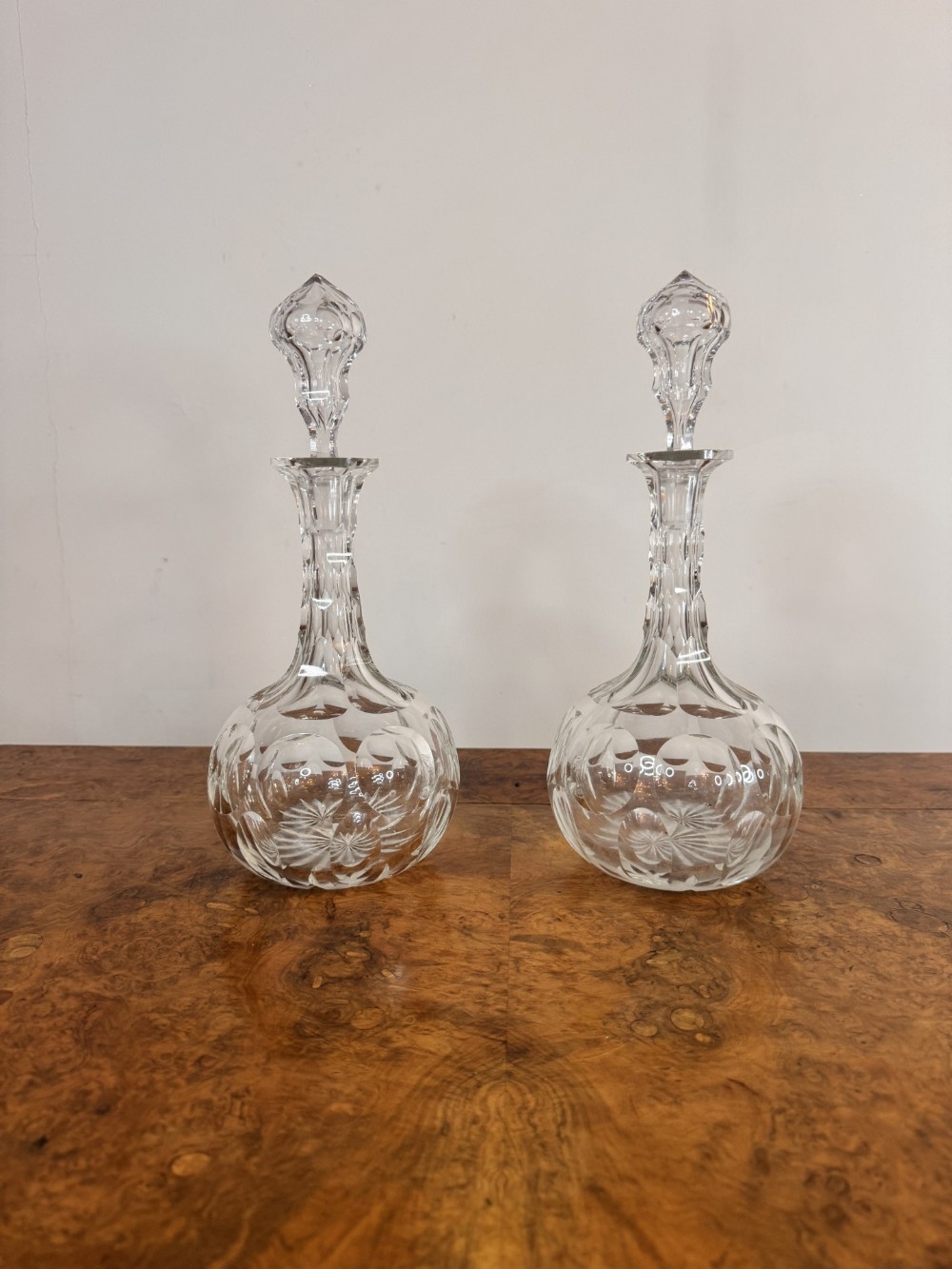 A pair of clear Edwardian cut glass decanters featuring rounded bulbous bodies, faceted necks, and matching glass stoppers.