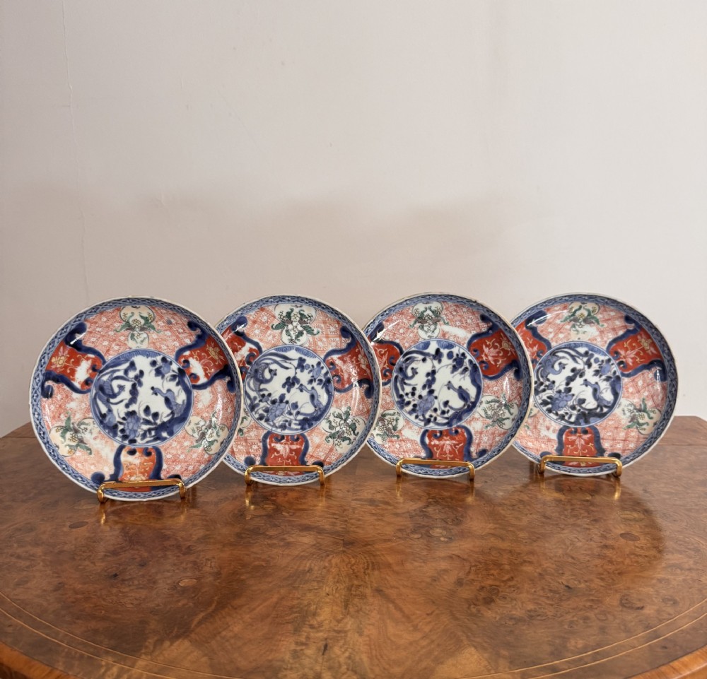 A set of four small round Japanese Imari porcelain plates featuring hand-painted cobalt blue and iron-red floral and bird patterns.