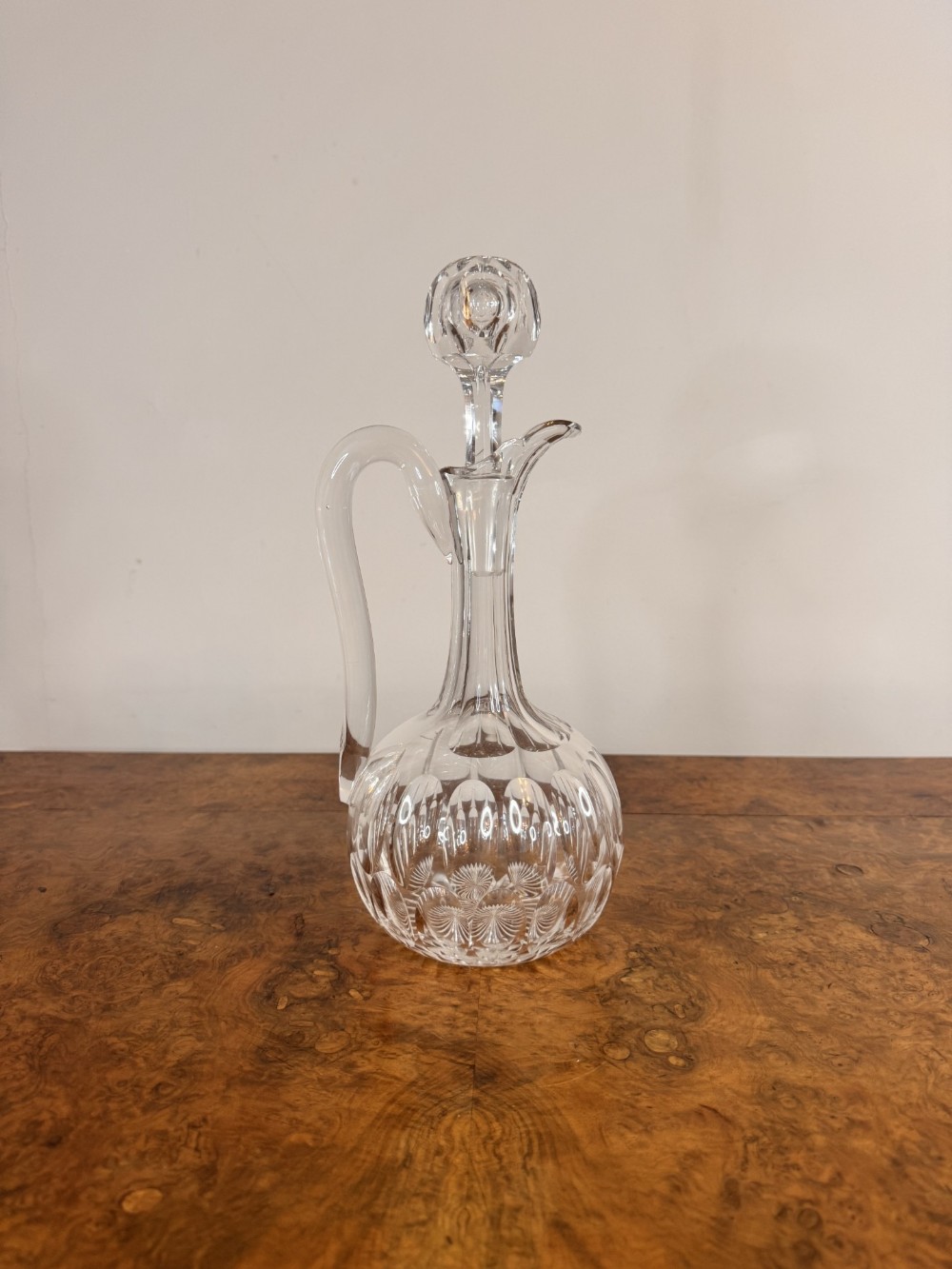 An Edwardian clear cut glass ewer featuring a high loop handle, decorative geometric cuts, a narrow neck, and a matching faceted glass stopper.