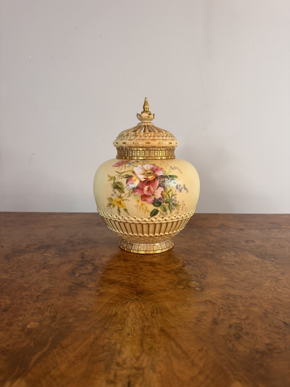 An antique Victorian Royal Worcester blush ivory porcelain potpourri jar with hand-painted floral patterns, a reticulated lid, and gilded relief details.