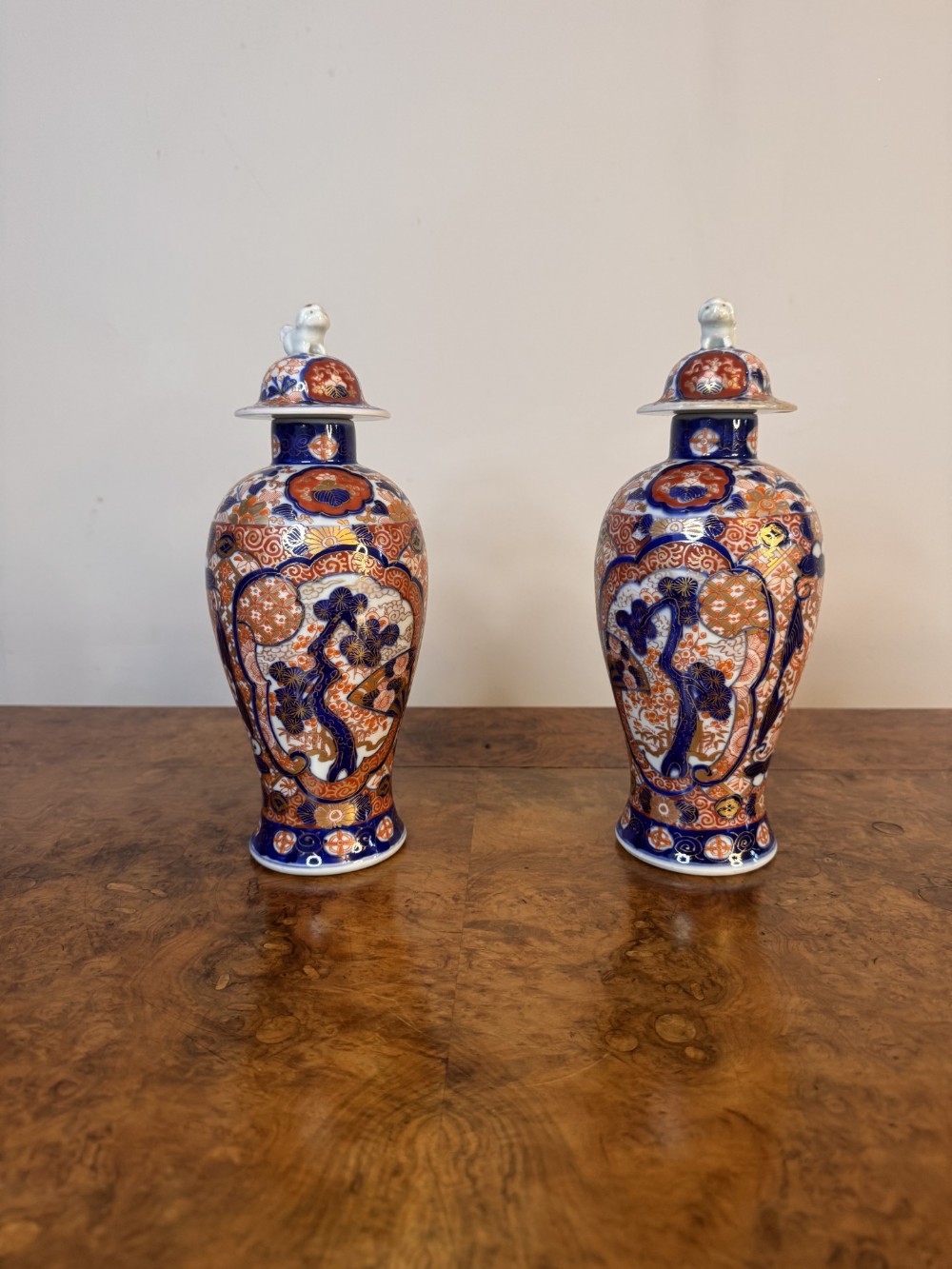 A pair of 19th-century Japanese Imari porcelain lidded vases decorated with cobalt blue, iron-red, and gold floral patterns topped with small animal finials.