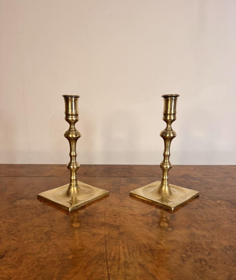 A pair of antique George II cast brass candlesticks featuring turned baluster stems and square bases.