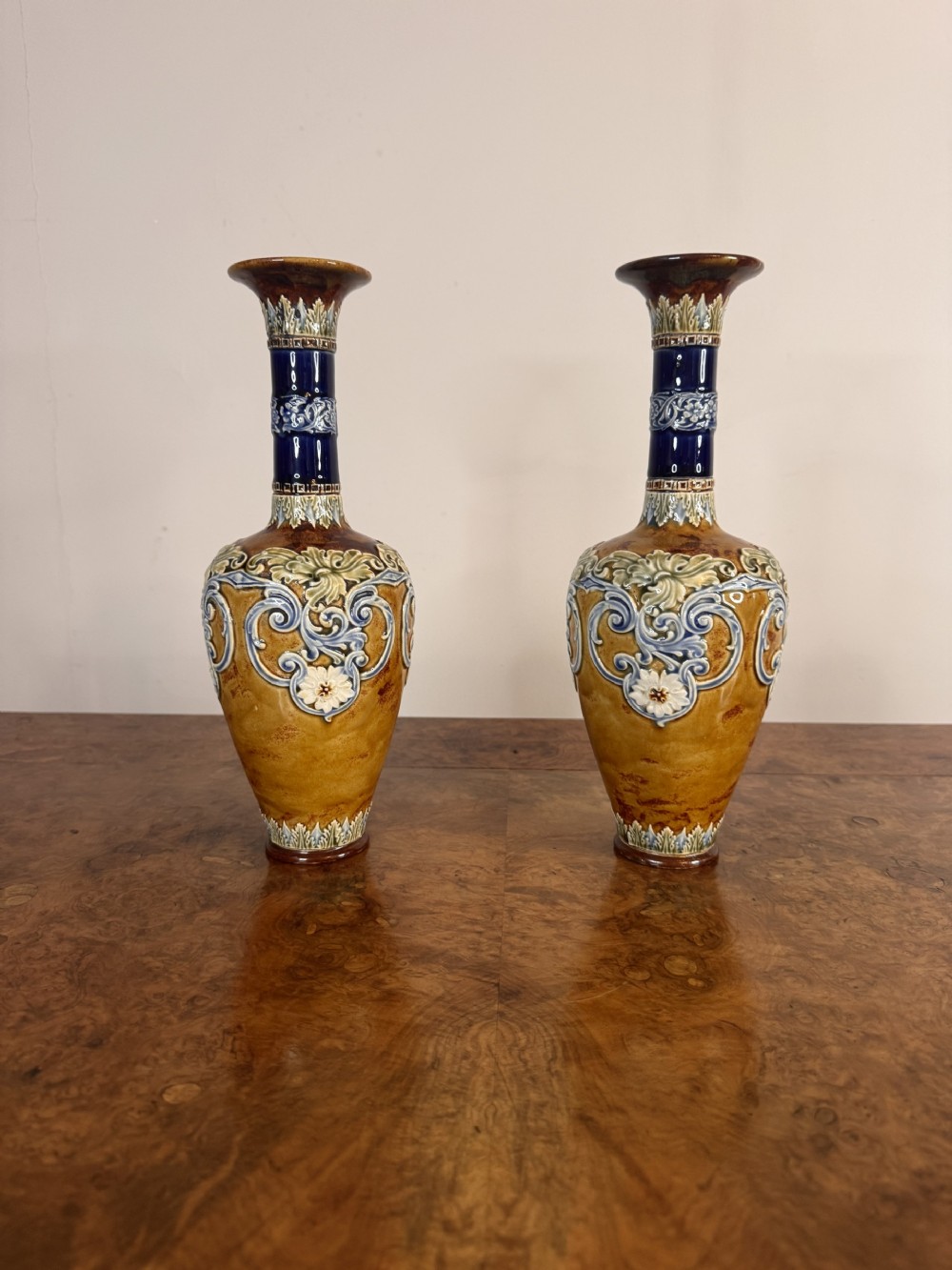 A pair of slender Victorian Doulton Lambeth glazed stoneware vases featuring floral relief scrolling in blue, brown, green, and white.