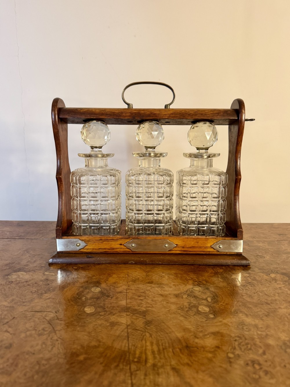 A Victorian oak tantalus housing three square cut-crystal decanters with round faceted stoppers and silver-plated metal fittings.