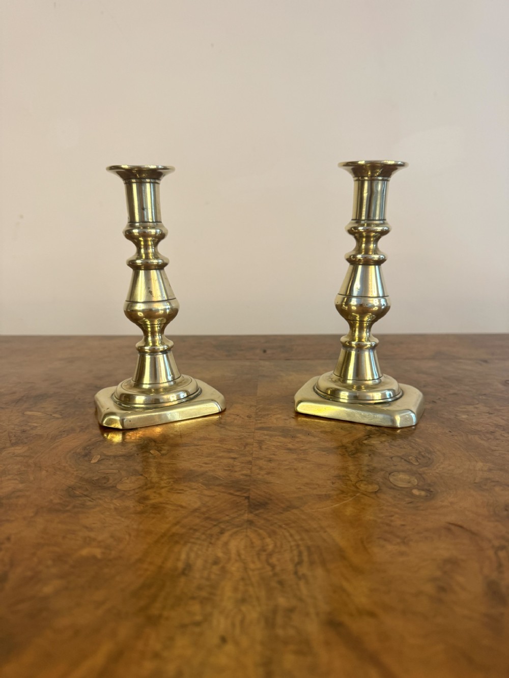A pair of polished Victorian brass candlesticks featuring turned knopped stems and square bases with stepped corners.