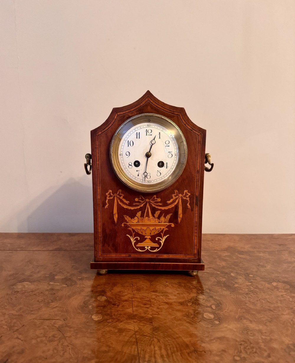 An Edwardian mahogany lancet mantel clock featuring intricate floral marquetry inlay, brass side drop handles, and a white circular dial.