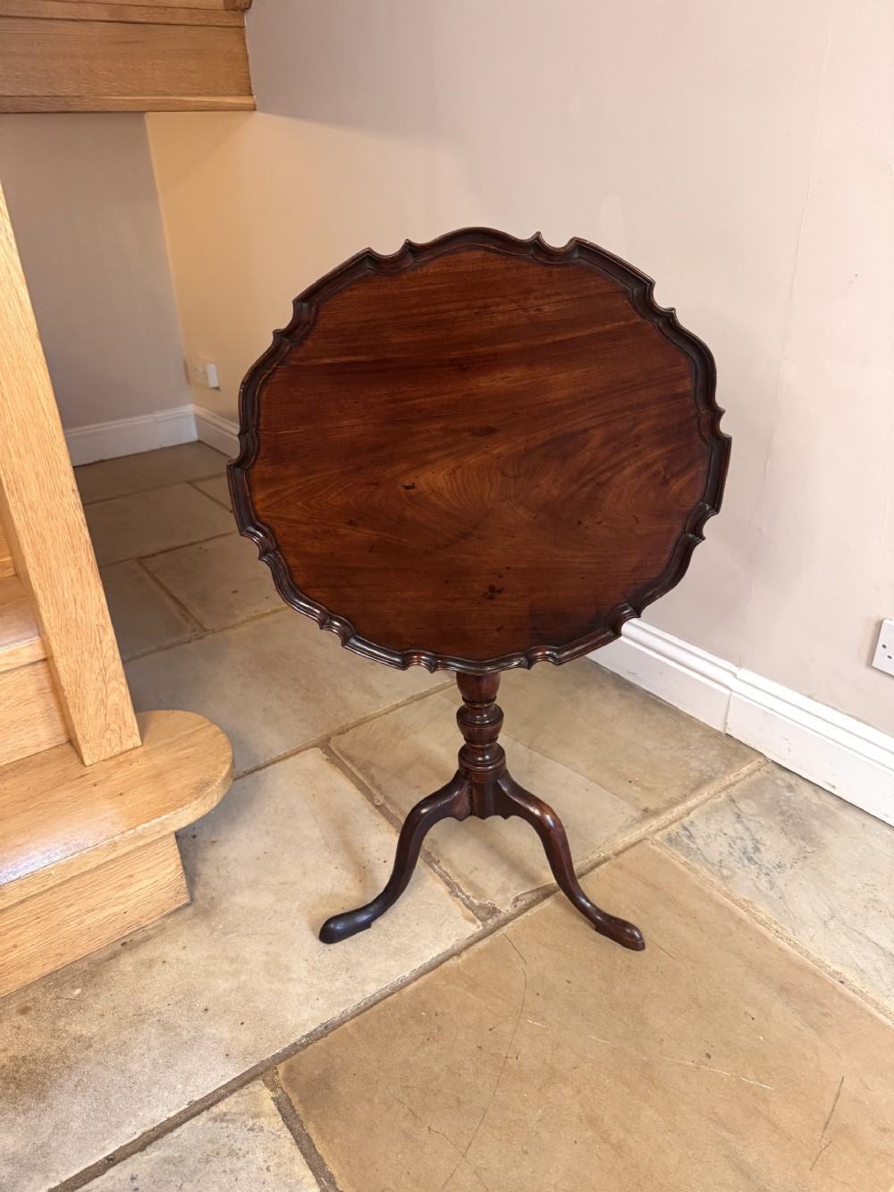 A George II mahogany tilt-top occasional table featuring a scalloped piecrust rim, turned central pedestal, and a tripod base, shown tipped vertically.
