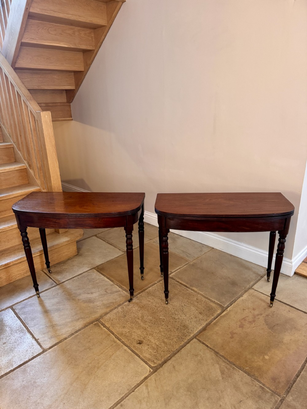 A pair of Regency mahogany fold-over tea tables with D-shaped tops and turned tapering legs terminating in brass castors.