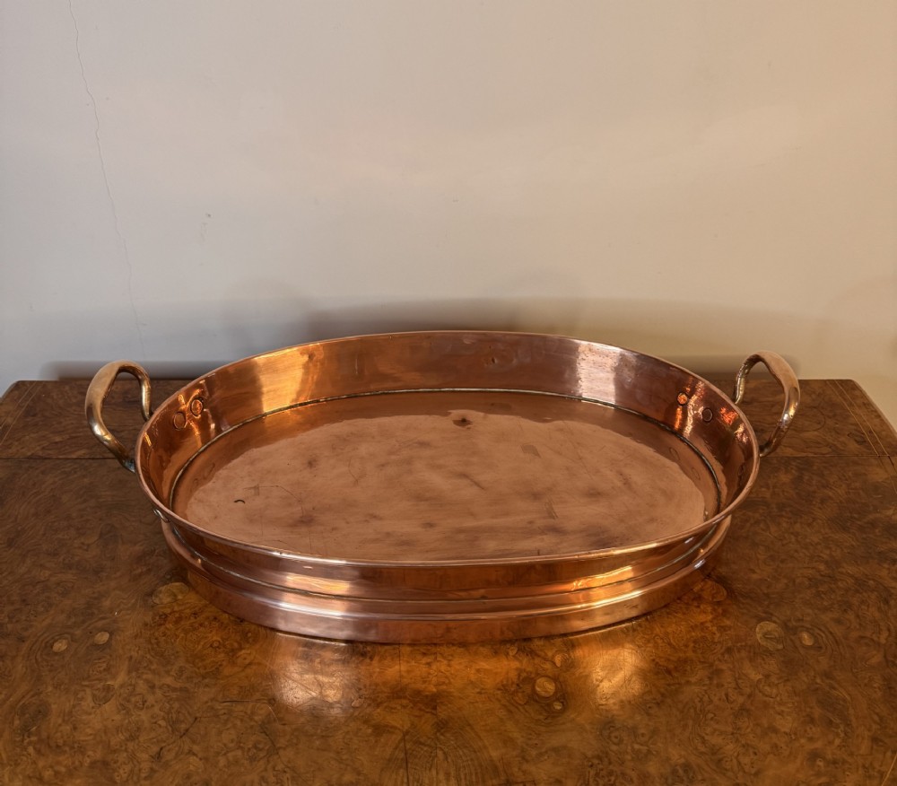 An oval Victorian copper pan featuring polished sides, a flat base, and two cast side handles secured with copper rivets. View II