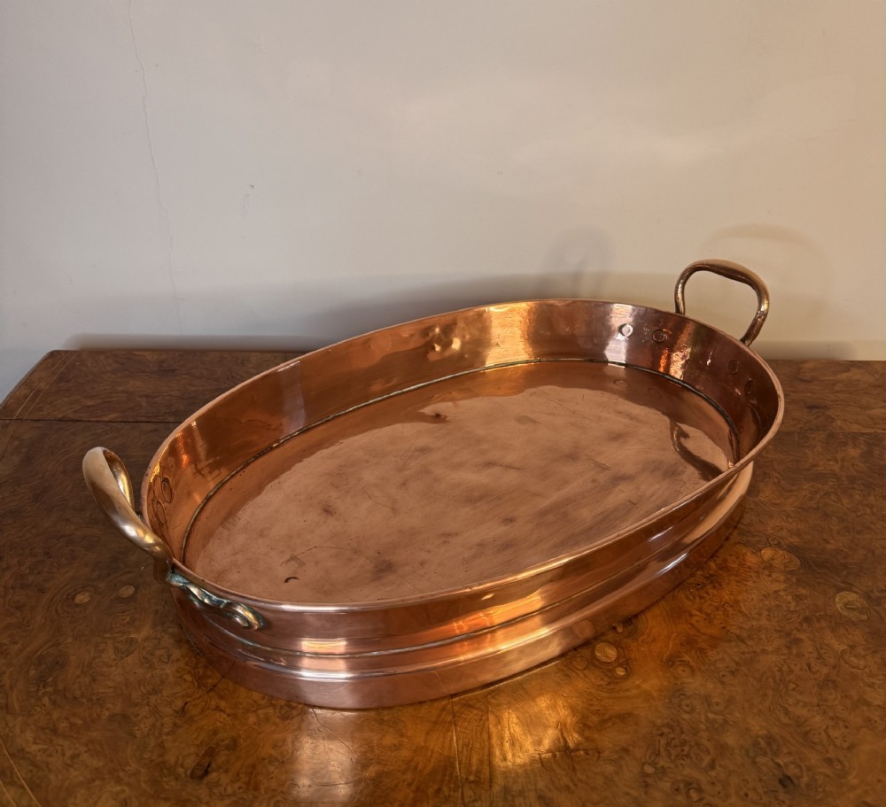 An oval Victorian copper pan featuring polished sides, a flat base, and two cast side handles secured with copper rivets. View III