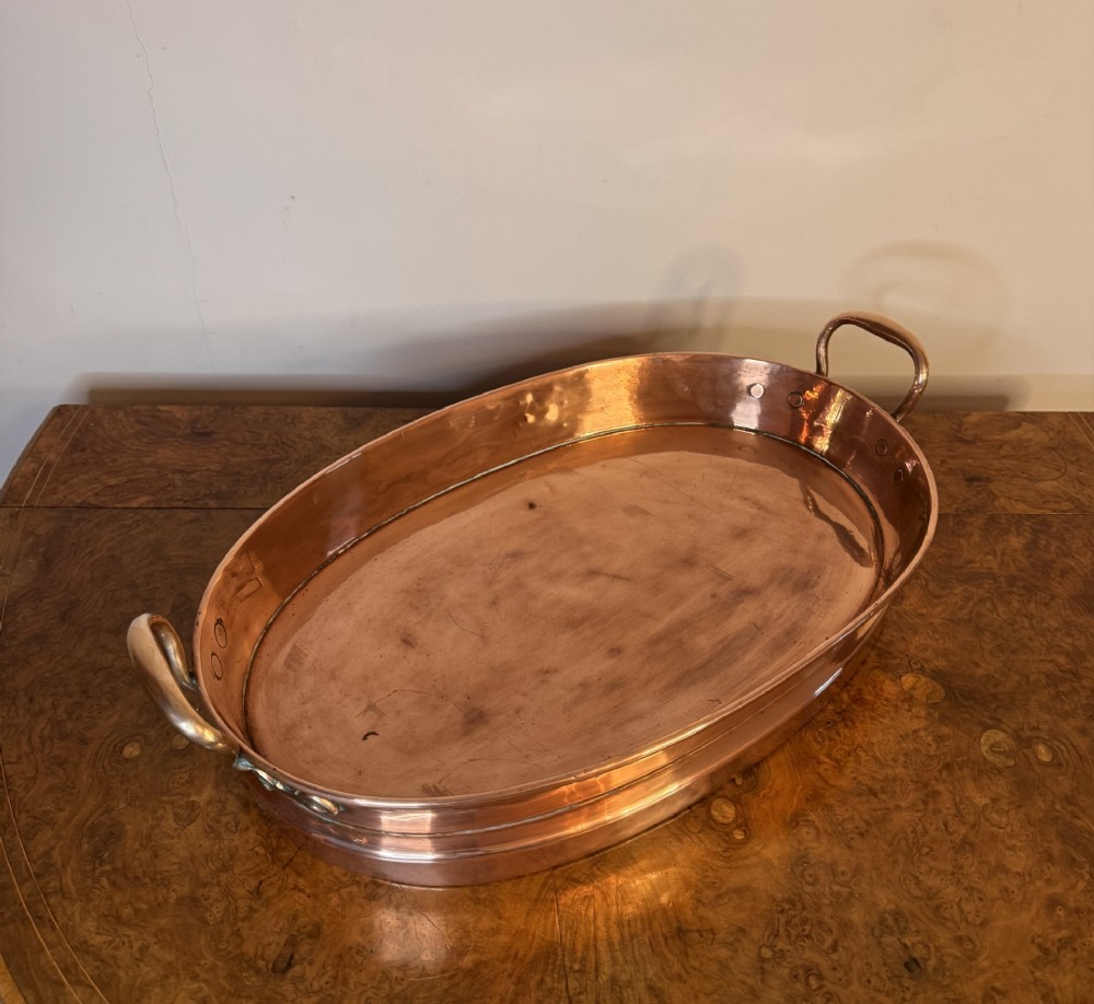 An oval Victorian copper pan featuring polished sides, a flat base, and two cast side handles secured with copper rivets. View IV