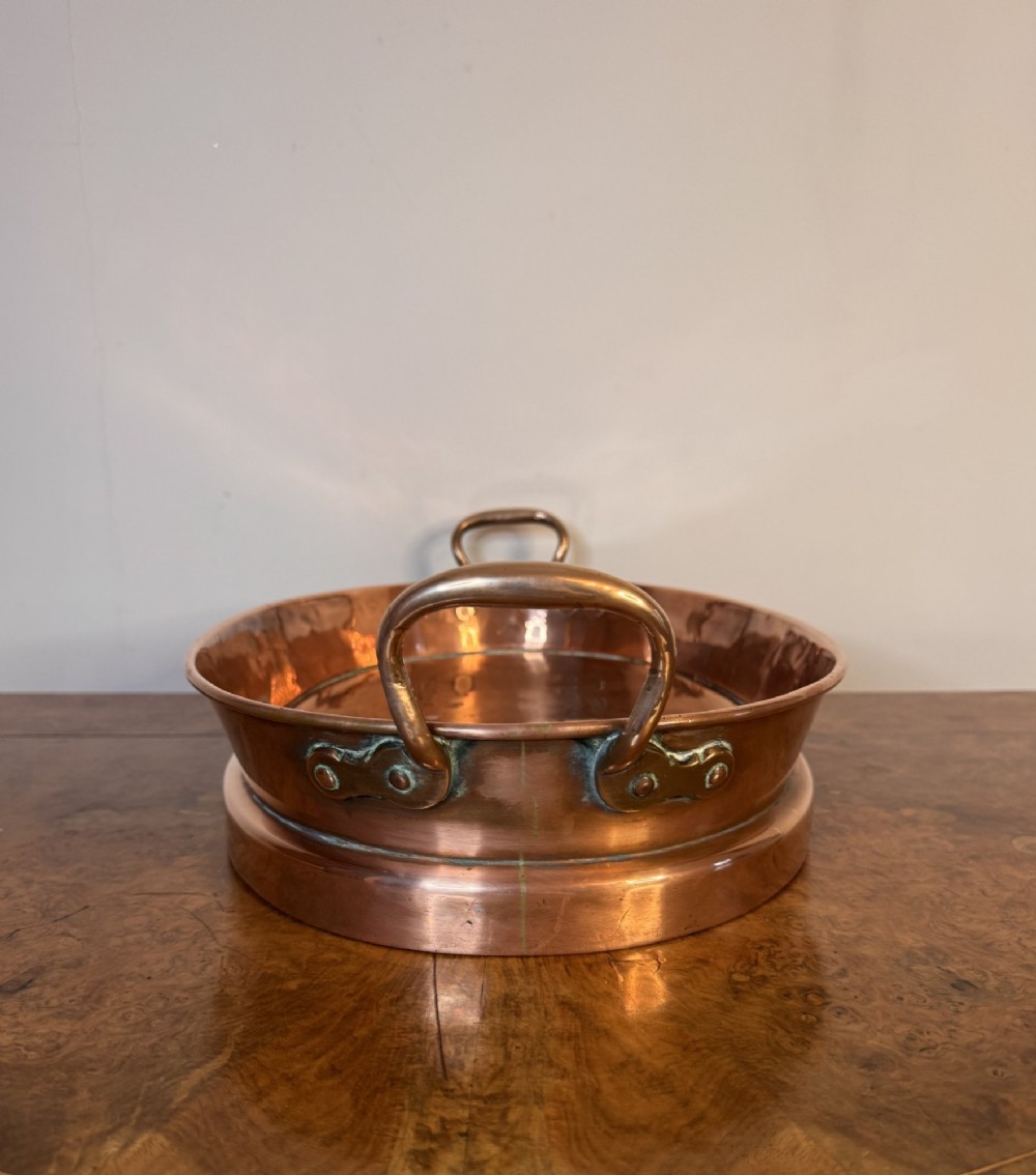 An oval Victorian copper pan featuring polished sides, a flat base, and two cast side handles secured with copper rivets. View V