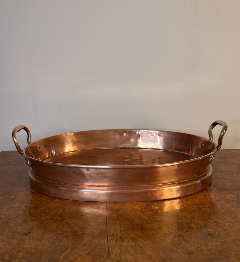An oval Victorian copper pan featuring polished sides, a flat base, and two cast side handles secured with copper rivets. View VIII