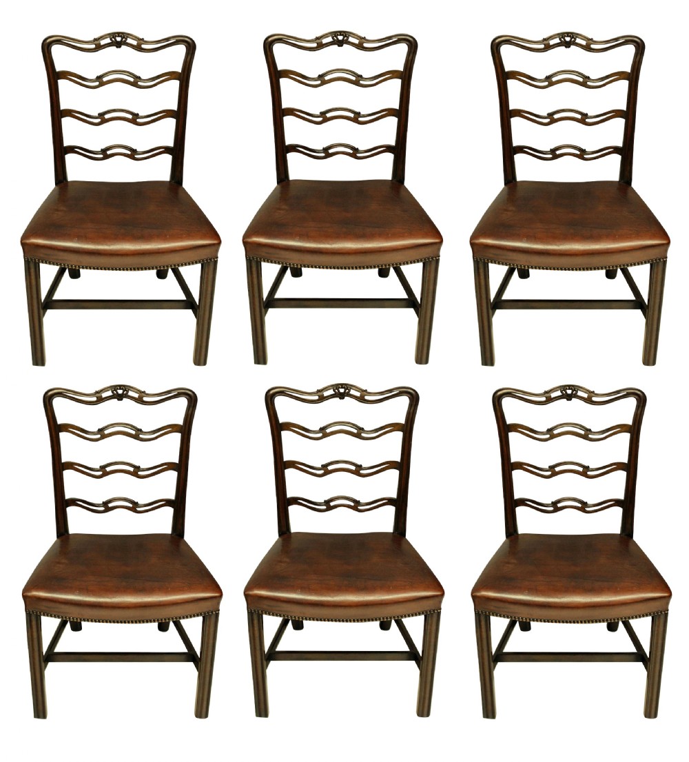 A set of six dark mahogany George III style ladderback dining chairs with brass-studded brown leather seats.