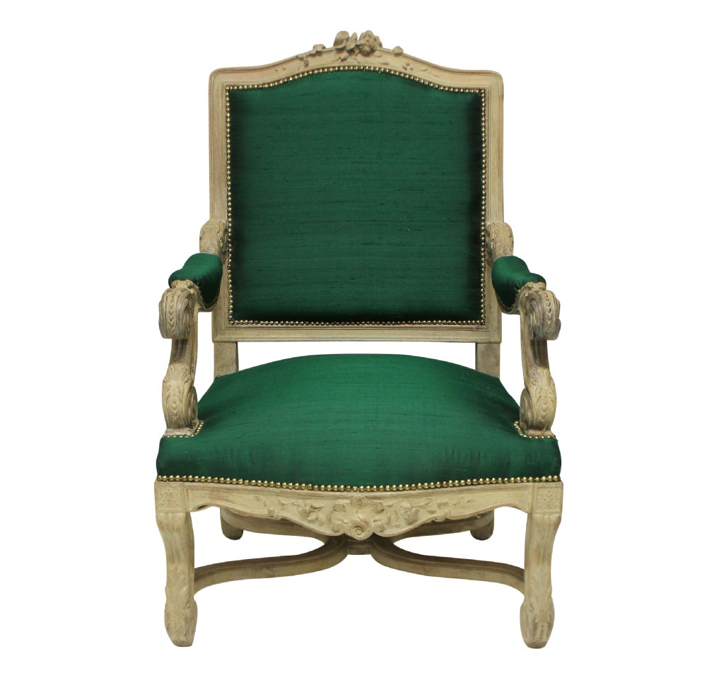 A Louis XIV style carved wood armchair upholstered in vibrant emerald green silk with brass stud details.