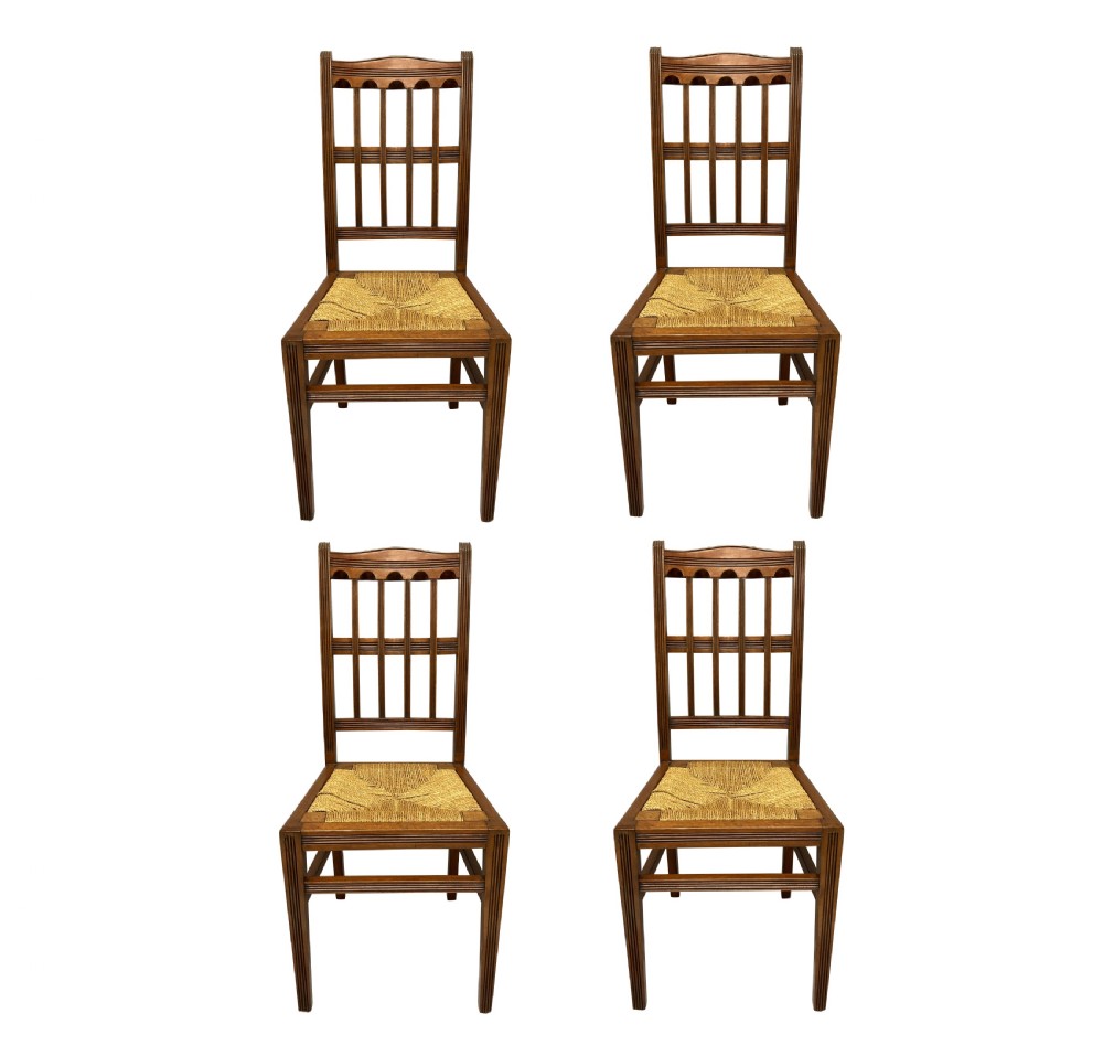 A set of four English Aesthetic Movement mahogany dining chairs featuring vertical spindle backs and natural rush woven seats.