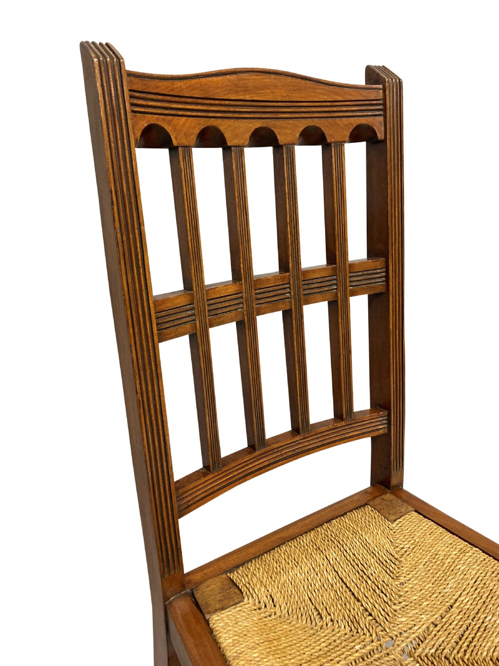 A set of four English Aesthetic Movement mahogany dining chairs featuring vertical spindle backs and natural rush woven seats. View IV